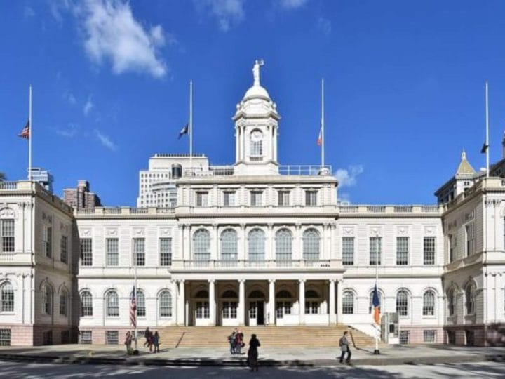 A wide, white building with grand architecture, as people roam in front of it.
