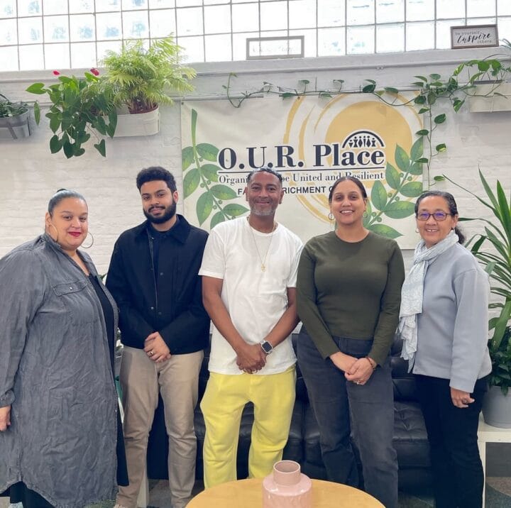 4 people stand shoulder to shoulder in front of "O.U.R Place" sign