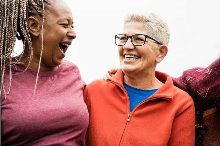 Two women, hugging side by side, and laughing.