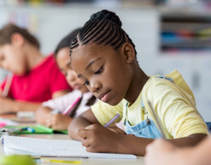 10-year old student sitting at a desk holding a pencil, writing on a piece of paper