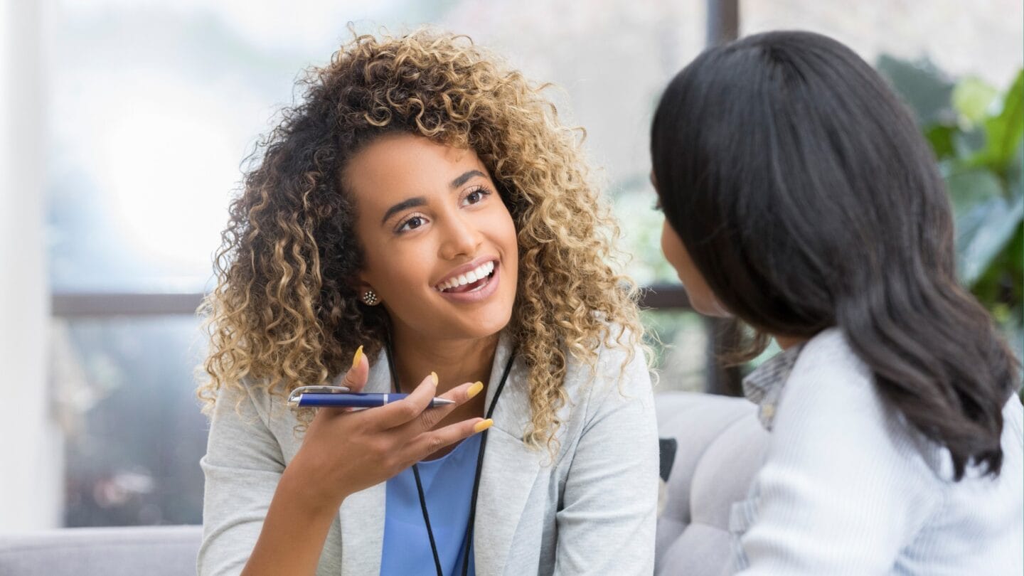 Two women sitting on a couch in conversation with one another.